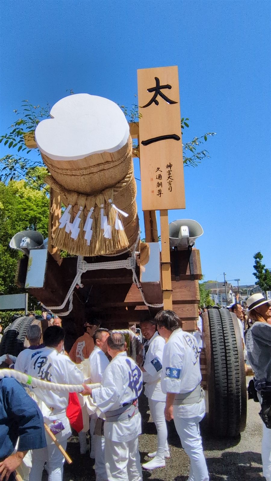 「太一」の御札を掲げた奉曳車と、白装束で綱を握る奉曳の人々。晴れた青空の下、伊勢のお木曳行事にて。
